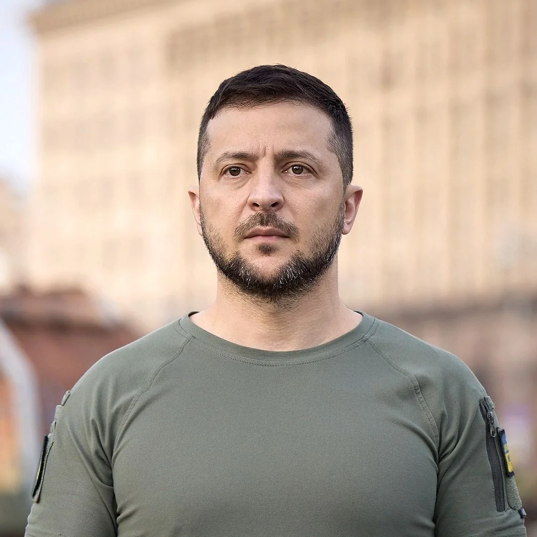 Портрет Володимира Зеленського в оливковій футболці з шевроном України на розмитому міському фоні