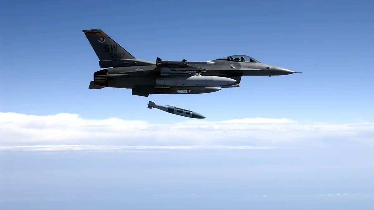 Сірий винищувач F-16 скидає бомбу над хмарами у блакитному небі