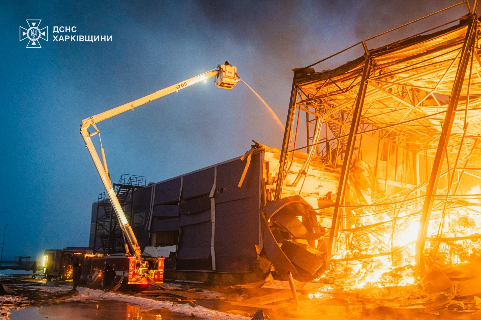 Пожежна автодрабина гасить пожежу на пошкодженій промисловій будівлі вночі