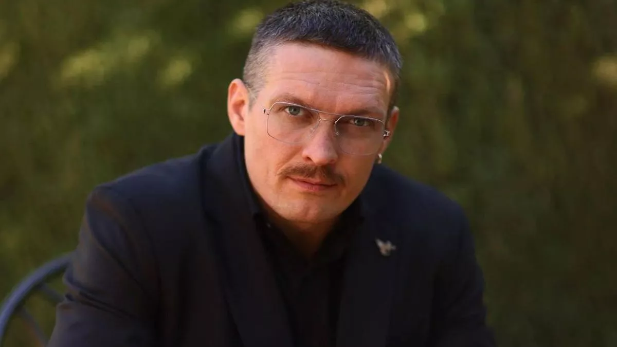 Олександр Усик у чорному костюмі та окулярах дивиться в камеру на природі