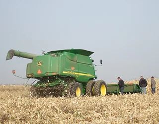 Зелений комбайн John Deere збирає врожай на сухому полі з людьми поруч