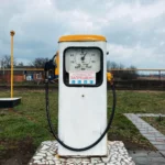 Стара біла бензоколонка з жовтим дахом, шлангами та механічним лічильником під хмарним небом